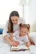© etonastenka - Close-up mom and little daughter are resting in a cozy bed, reading a funny interesting children's book together