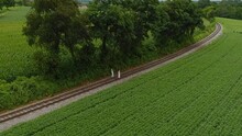 An Aerial View Of Two Amish Girl Walking On A Single Rail Road Track In The Middle Of Amish Farm Lands