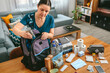 © David Pereiras - Woman putting cans of food to prepare emergency backpack in living room