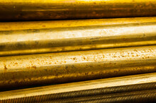 Large Bronze Round Bars And Steel Threaded Rods Lie On A Shelf, Close-up.