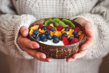 Healthy breakfast. Woman holding coconut bowl with yogurt, corn flakes, sliced kiwi and berry fruit. Dieting food for wellbeing and good vitality