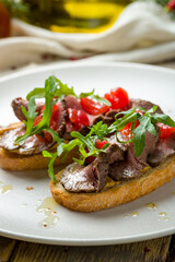 Poster - Bruschetta with roast beef, tomatoes and aragula on white plate, vertical, macro close up