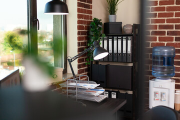 Wall Mural - Close up of desk and bookshelf with decorations in office. Empty table with documents and computer, shelves with minimal decor. Water dispenser and bookcase with ornaments and plants.