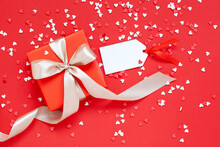 Valentines Day Concept. Red Gift Box With Beautiful Ribbon With Little Red And White Hearts On Red Background With Empty Tag For Text.