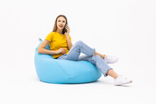 Young Surprised Woman Sitting On Bean Bag Talking On The Phone On White Background