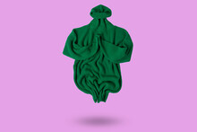 Green Long Sweater Levitates, Folded As If Meditating, Concept, On A Lilac Background