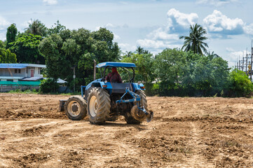 Wall Mural - Farmer driving a blue tractor to plowing cultivated soil