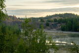Fototapeta Las - Early morning in an abandoned flooded clay quarry. Beautiful clouds, steam above the water.