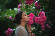 Beautiful tender woman enjoying with a scent of pink roses at the garden
