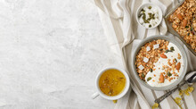 Cooked granola muesli with yogurt, pumpkin seeds, almonds and coconut pieces in baking sheet and bouls with a spoon and herbal tea. Flat lay of breakfast, top view with copy space
