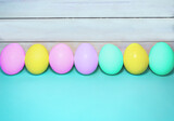 Fototapeta  - A line of multicolored Easter eggs on a wooden and turquoise background.