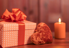 A Gift Box With A Red Plush Heart And A Burning Candle On A Pink Wooden Background. Selective Focus.