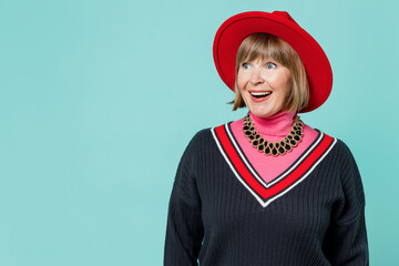 Wall Mural - Elderly smiling shocked amazed fun caucasian woman 50s wearing necklace shirt red hat look aside on workspace isolated on plain pastel light blue background studio portrait. People lifestyle concept.