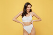 © ViDi Studio - Smiling attractive young brunette woman 20s in white underwear with perfect fit body stand akimbo posing look aside on workspaece area mock up put hands on waist isolated on plain yellow background.