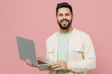 Wall Mural - Young smiling happy cheerful european man 20s wearing trendy jacket shirt hold use work on laptop pc computer isolated on plain pastel light pink background studio portrait. People lifestyle concept.