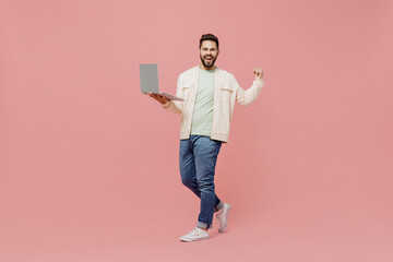 Full body young smiling happy man 20s wearing trendy jacket shirt hold use work on laptop pc computer do winner gesture isolated on plain pastel light pink background studio. People lifestyle concept.