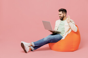 Sticker - Full body young man 20s wear trendy jacket shirt sit in bag chair use laptop pc computer waving hand talk by video call isolated on plain pastel light pink background studio. People lifestyle concept.