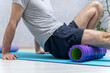 Man sits on yoga mat and doing massage his feet with foam roller. Workout at home. Roller for physiotherapy.