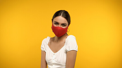 Wall Mural - Brunette woman in blouse and protective mask looking at camera isolated on yellow.