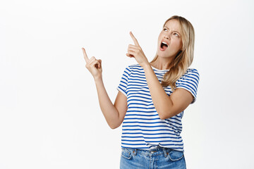 Wall Mural - Frustrated young stylish girl pointing left and complaining, looking disappointed and confused, standing over white background