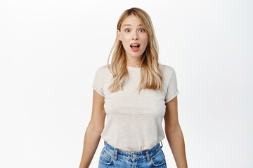 Wall Mural - Portrait of blond girl looking surprised and amazed, saying wow, staring with thrilled face expression, white background
