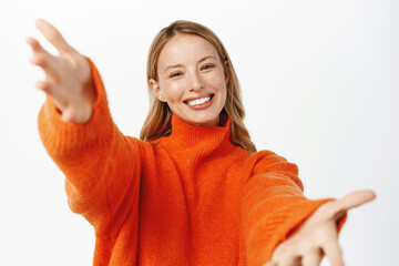Wall Mural - Portrait of beautiful blond girl smiling, reaching hands forward, stretching arms to hold, receive smth, hugging gesture, standing over white background