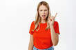 Angry young woman, disapprove smth bad, scolding, shaking finger at you, prohibit, dislike something, standing in red tshirt over white background