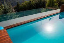 Infinity Swimming Pool With Glassy Safe Fence And Hardwood Decking Overlooking Landscape