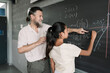 © Tamia Studio - Maths lesson in a secondary school. Latin Female Teenager Student writing on Blackboard with help of friendly teacher in High School.