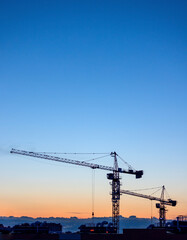 silhouettes of tower cranes on construction site at sunset