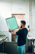 © Zamrznuti tonovi - Male worker holds the silkscreen frame in a printing workshop
