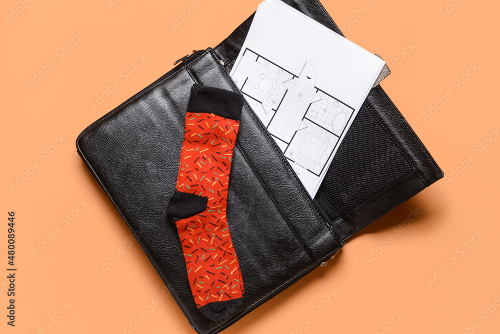 Briefcase with drawings and sock on color background