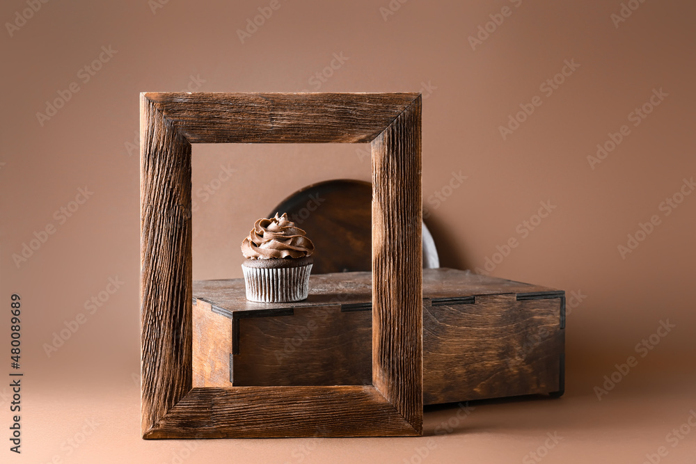 Tasty chocolate cupcake with wooden box and frame on color background