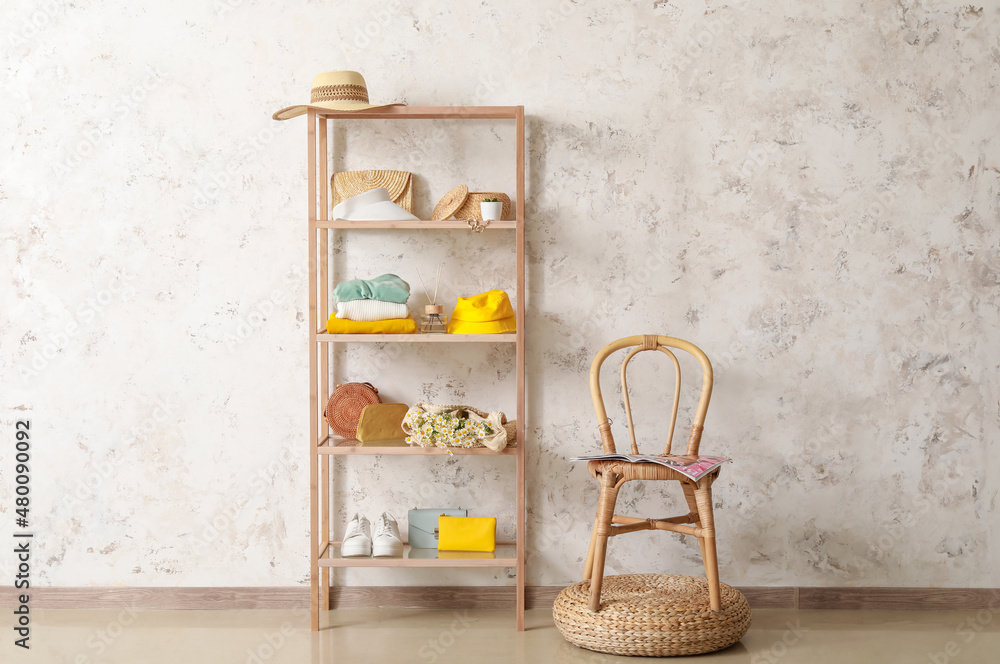 Shelving unit with accessories, chair and pouf near light wall