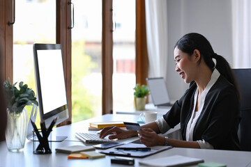 Side view smiling businesswoman holding credit card and using computer for banking online.