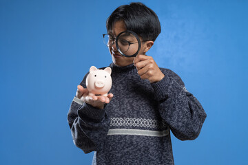 young man looking piggy bank with a magnifying glass