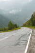 A picturesque view of the bend of the hairpin of a wet winding road through the pass, part of a mountain serpentine in cloudy weather with fog, mountain road on a rainy day. selective focusing