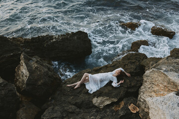 Poster - Beautiful bride Lies on his back on a stone cliff, cloudy weather view from above