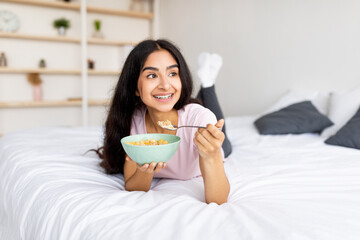portrait of fit indian lady eating cereal with milk on bed at home, taking care of her body