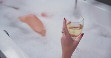 Closeup Young Caucasian Girl In Bubble Bath Drinking White Wine. Woman Leg Knee Hand With Glass.