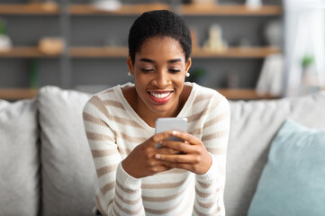 Cool App. Cheerful Young Black Woman Relaxing On Couch With Smartphone