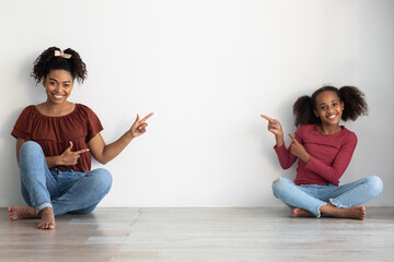 Wall Mural - Cheerful african american mother and daughter pointing at copy space