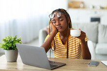 Exhausted Black Woman Sitting In Front Of Laptop, Drinking Coffee