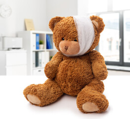 Wall Mural - medicine, healthcare and childhood concept - teddy bear toy with bandaged head having toothache over medical office at hospital background