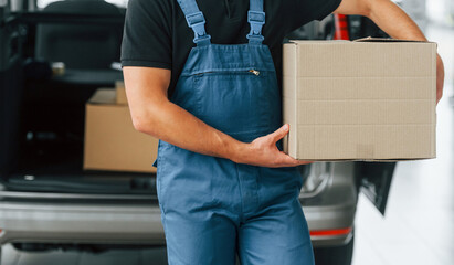 Business of service. Delivery man in uniform is indoors with car and with order