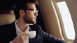 © LIGHTFIELD STUDIOS - Bearded businessman in eyeglasses holding cup in private jet.