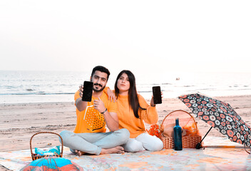 Wall Mural - casual happy couple showing cellphone on beach indian pakistani model