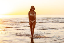 People, Summer And Leisure Concept - Happy Smiling Young Woman In Bikini Swimsuit On Beach Over Sunset