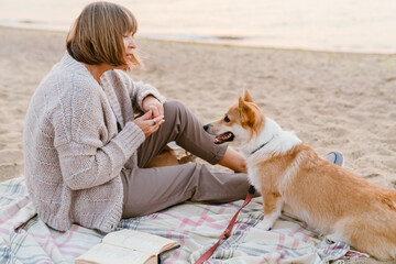 Senior woman reading book while resting with her dog on beach