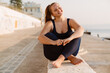 © Drobot Dean - Young ginger woman smiling during yoga practice at seafront